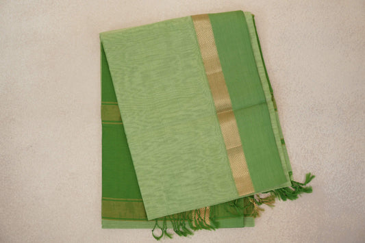 Folded pista green Maheshwari silk cotton saree with fine checks, a leaf green border, gold zigzag detailing and green tassels.