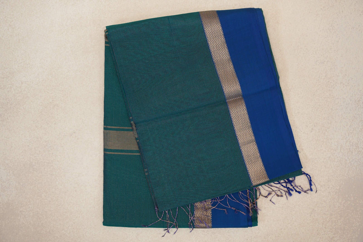 Folded teal green Maheshwari silk cotton saree with fine stripes, a royal blue border, gold zigzag detailing and tassels.