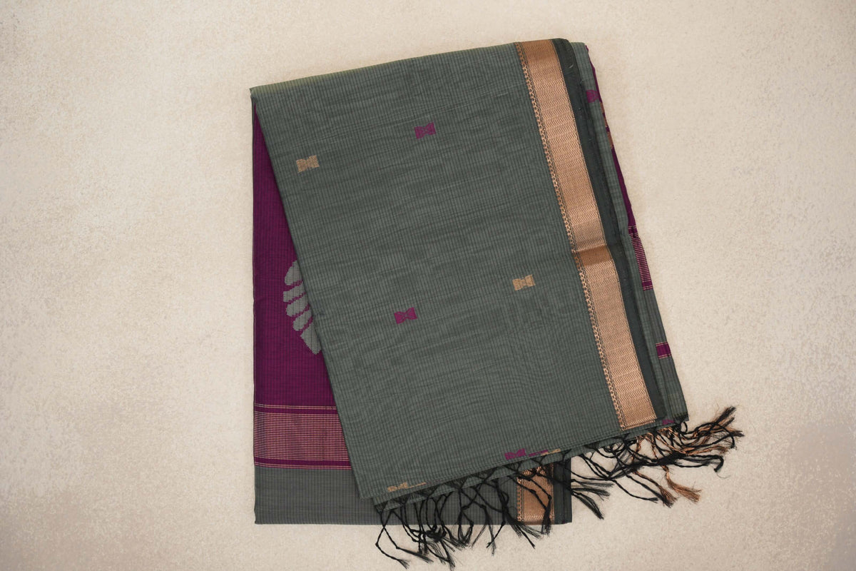 Folded sage green Maheshwari silk cotton saree with fine checks, small magenta and gold motifs, a deep sage and gold border, and dark tassels.