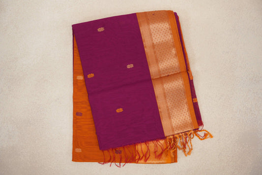 Folded dark magenta Maheshwari silk cotton saree with small scattered motifs, a deep orange geometric-woven border and orange tassels.
