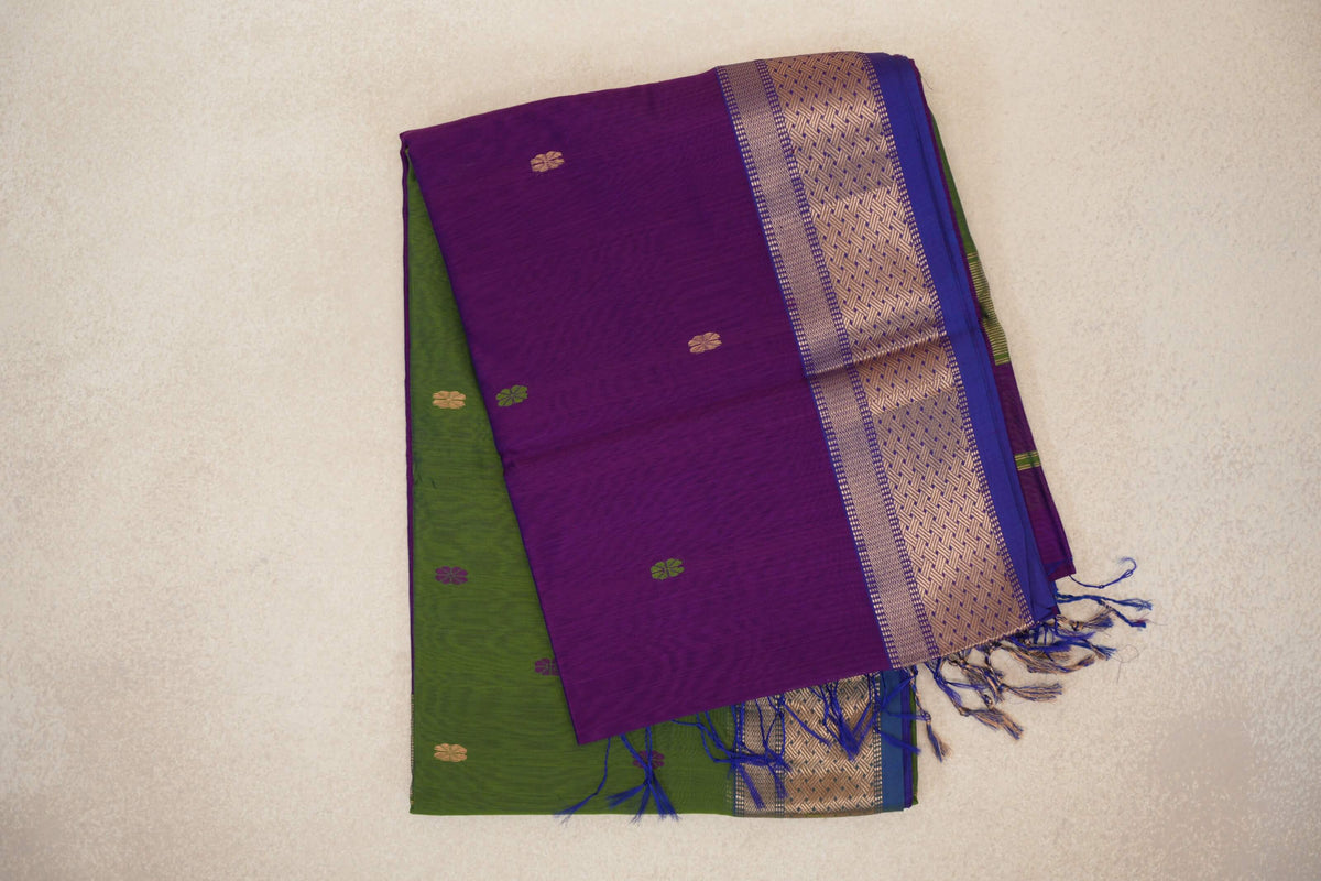 Folded Maheshwari silk cotton saree with a violet purple body, small scattered motifs, a gold-patterned royal blue border, olive green layer and tassels.