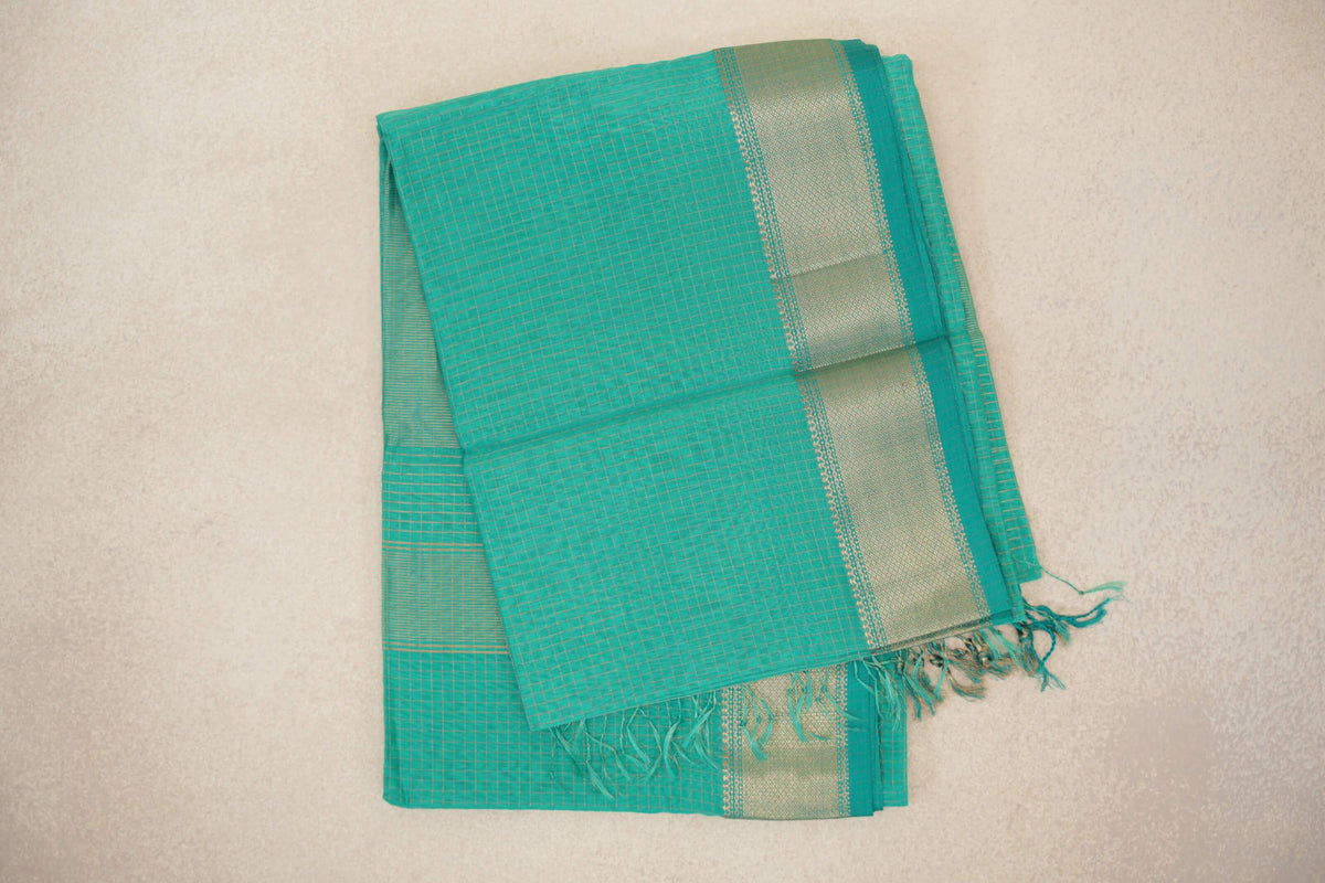 Folded turquoise green Maheshwari silk cotton saree with fine checked lines, a gold-toned woven border and tassels at the end.