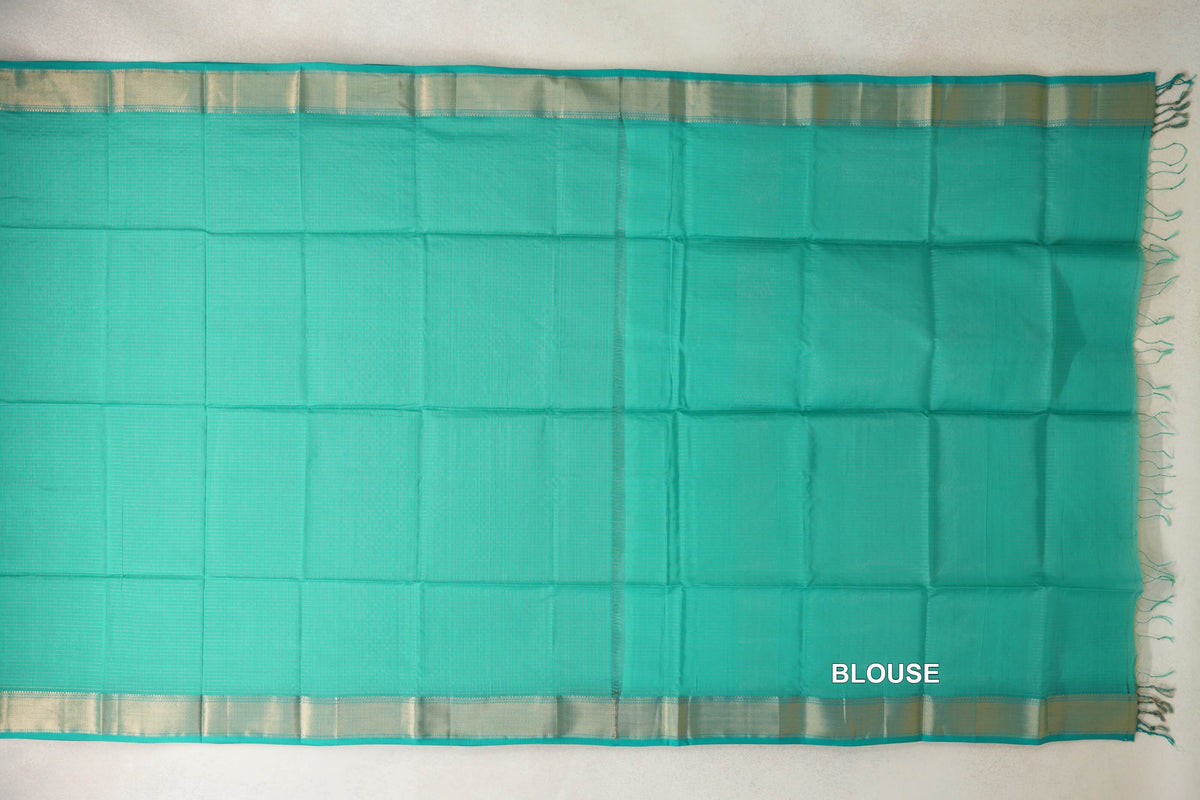 Turquoise green Maheshwari silk cotton saree laid flat, showing the plain body, matching blouse section, pale shimmering borders and tassels.