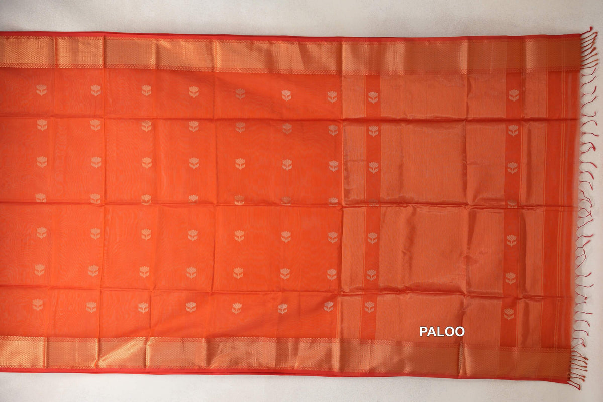 Reddish orange Maheshwari silk cotton saree laid flat, with small pale floral motifs, red-edged woven borders and a striped pallu with tassels.