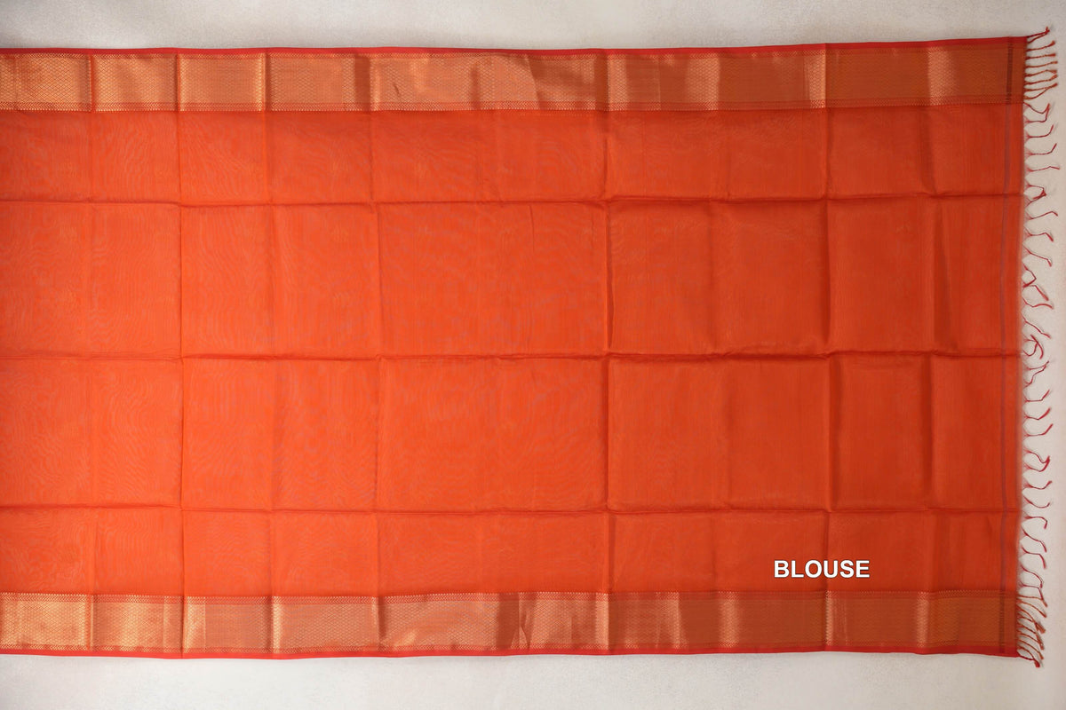Reddish orange Maheshwari silk cotton blouse fabric laid flat, with woven borders, red selvedge edges and tassels at one end.
