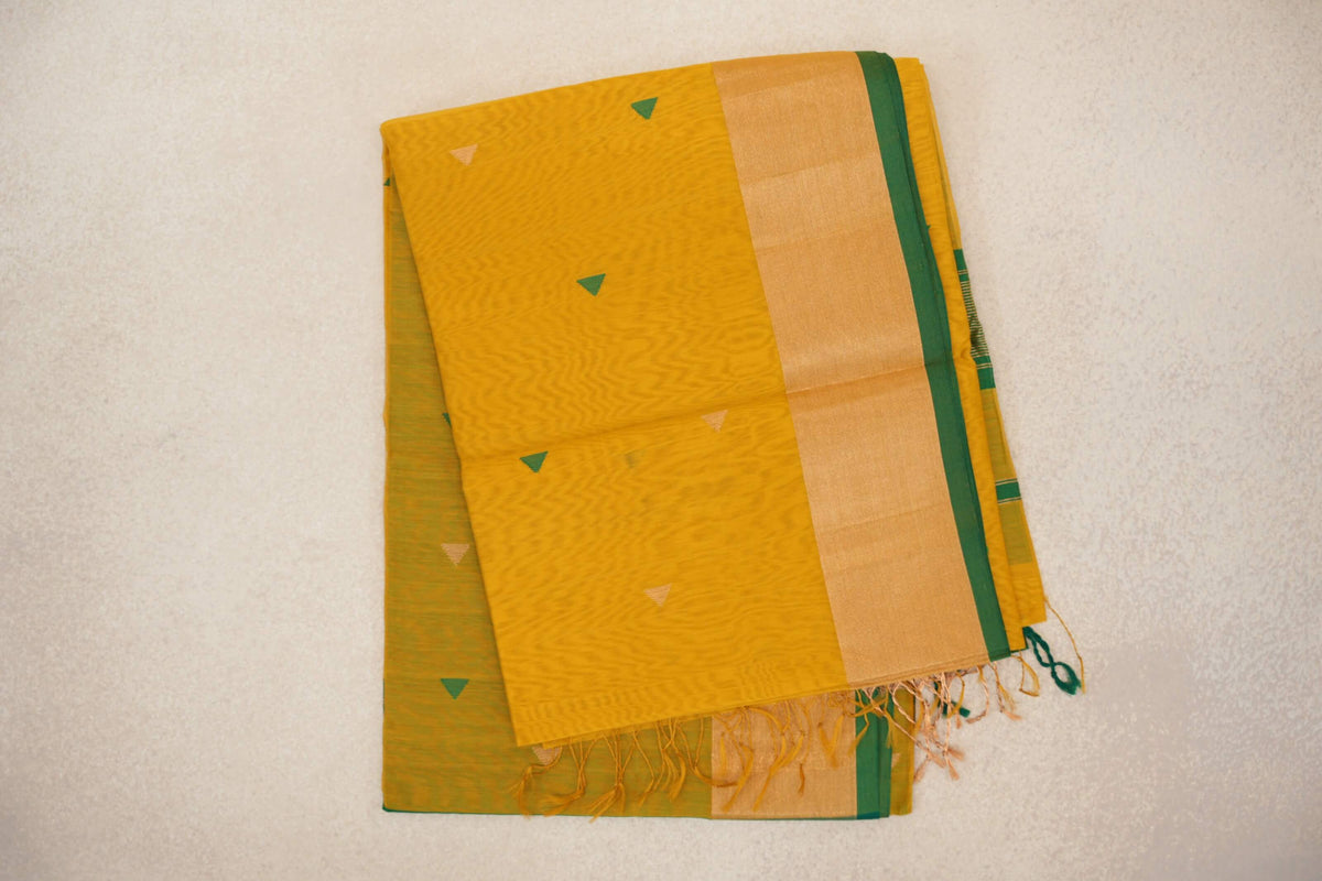 Folded turmeric yellow Maheshwari silk-cotton saree with small green and pale pink triangles, a broad light yellow border, bottle green edge and tassels.