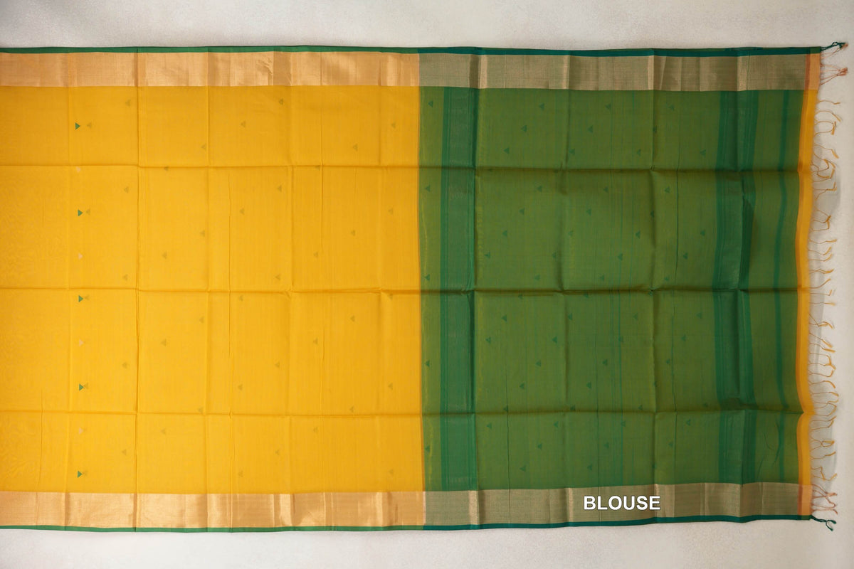 Turmeric yellow Maheshwari silk-cotton saree spread flat, with tiny triangle motifs, green-edged borders and a bottle green blouse section on the right.