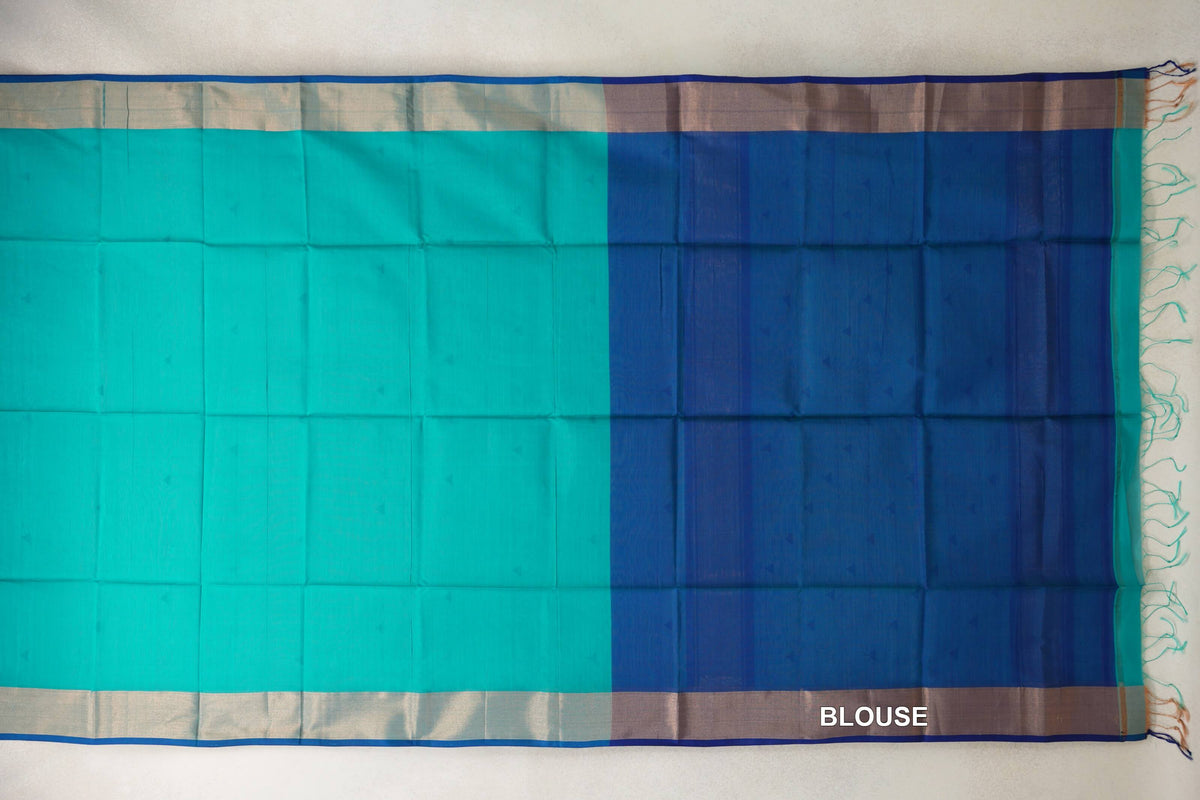 Maheshwari silk-cotton saree laid flat, with a bright turquoise green body, silver-toned borders, and a Classic Blue blouse section with tassels.