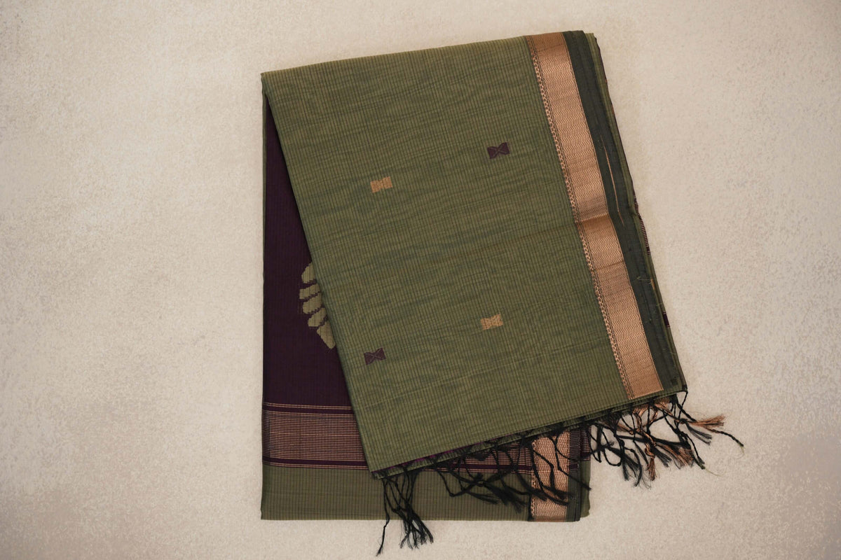 Folded muted olive green Maheshwari silk cotton saree with fine stripes, small geometric motifs, a copper-toned border and a deep wine plum pallu with tassels.