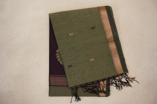 Folded muted olive green Maheshwari silk cotton saree with fine stripes, small geometric motifs, a copper-toned border and a deep wine plum pallu with tassels.