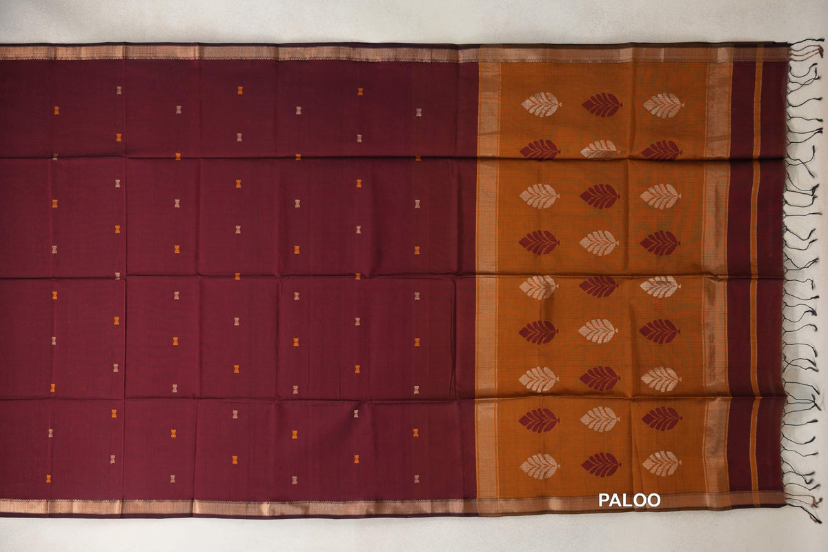Deep maroon Maheshwari silk cotton saree laid out with tiny motifs and narrow borders beside a deep mustard orange pallu with leaf patterns and tassels.