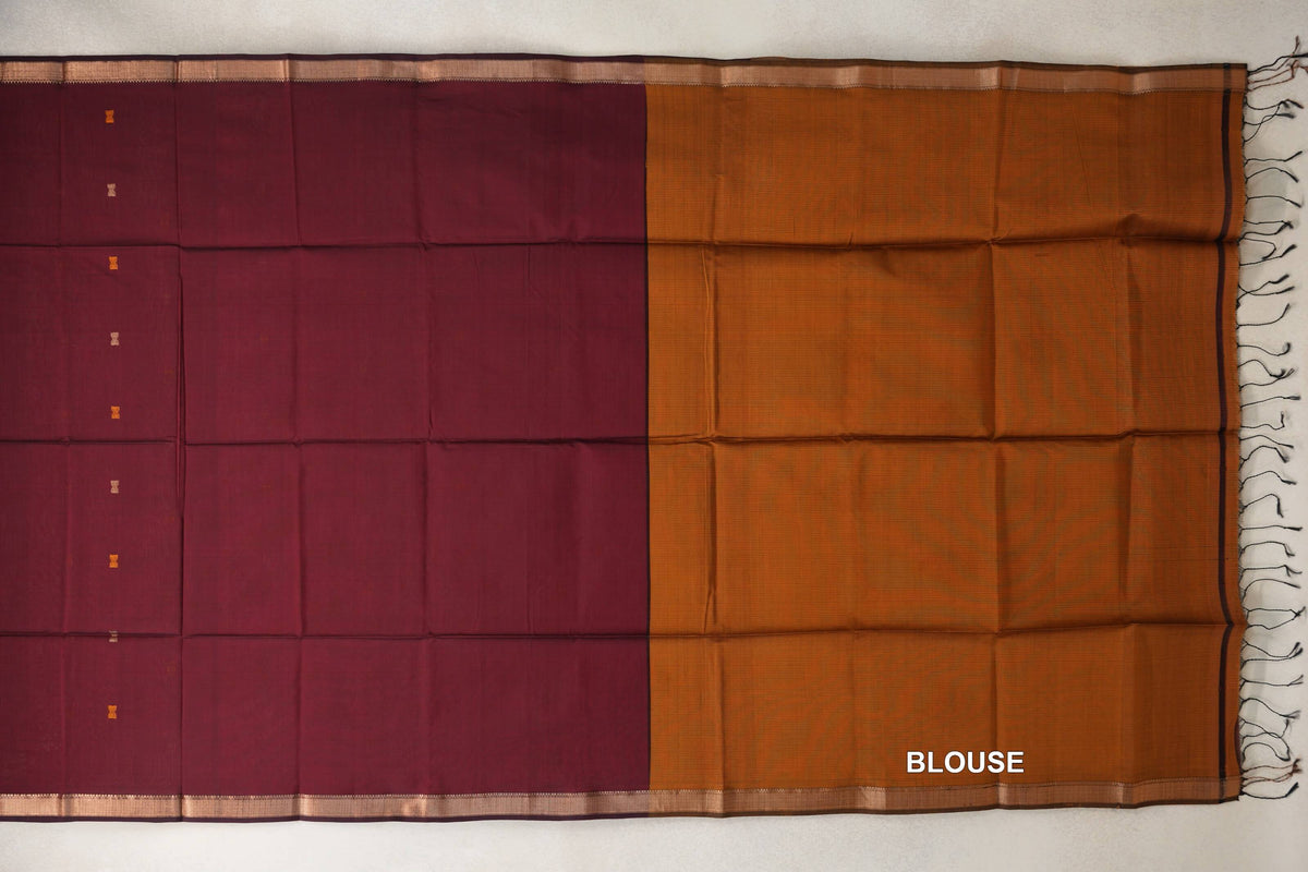 Maheshwari silk cotton saree laid flat, with a deep maroon body, small motifs and narrow borders beside a deep mustard orange blouse piece with tassels.