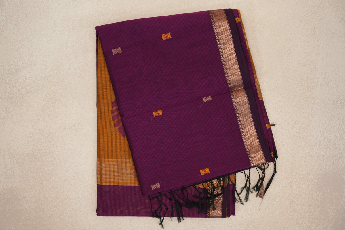 Folded deep magenta Maheshwari silk cotton saree with small geometric motifs, a patterned border, black tassels and a mustard orange layer beneath.