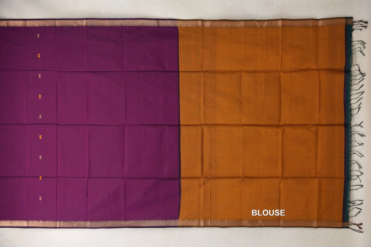 Spread-out Maheshwari silk cotton saree with a deep magenta body, small gold accents and narrow borders beside a deep mustard orange blouse piece with tassels.