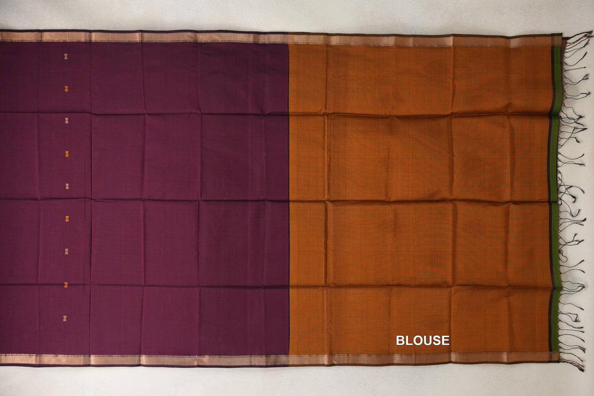 Laid-flat Maheshwari silk cotton saree with a deep wine body, small spaced motifs and copper-toned borders, beside a deep mustard orange blouse panel with tassels.