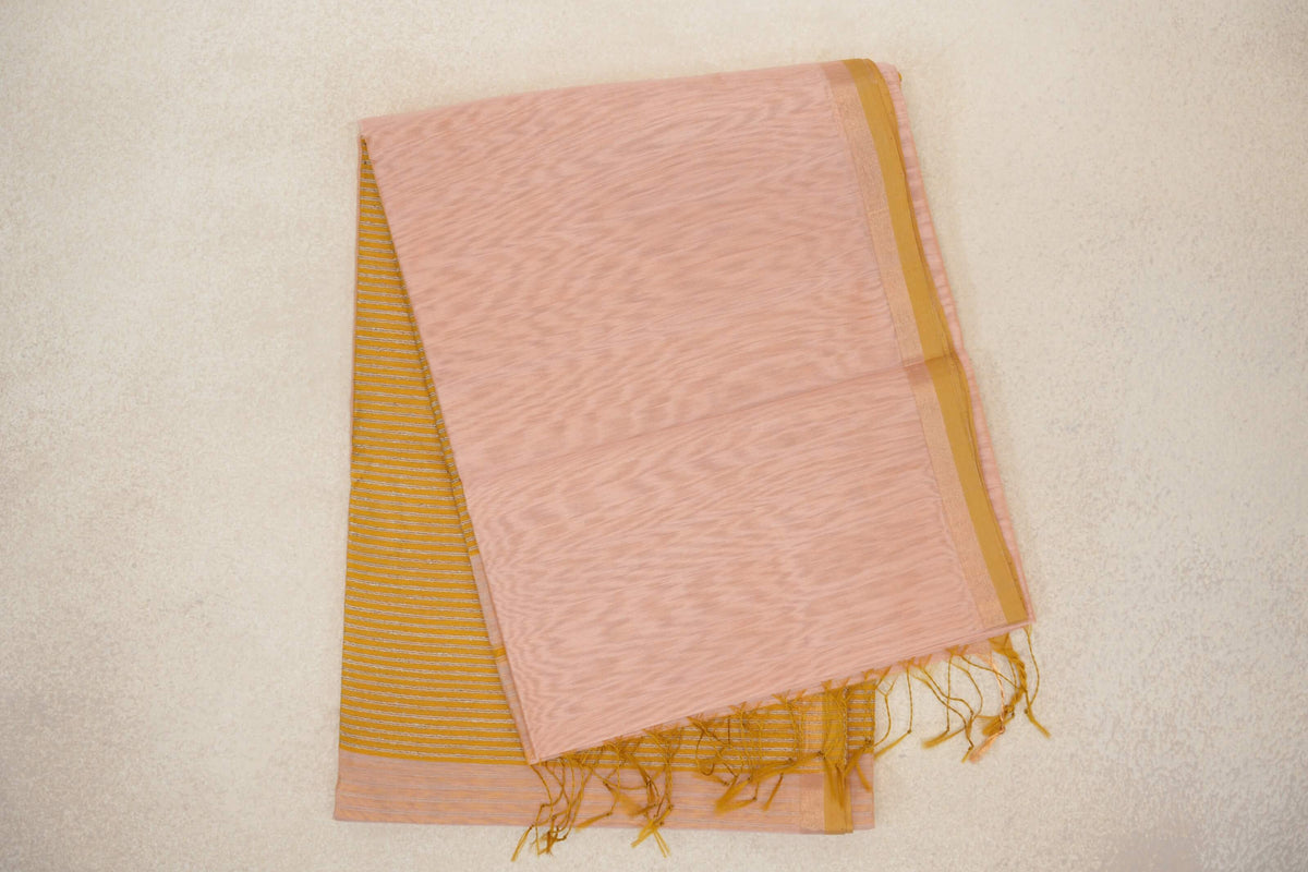 Folded peach Maheshwari silk cotton saree with a light mustard gold selvedge border, a striped section beneath and loose tassels at the end.
