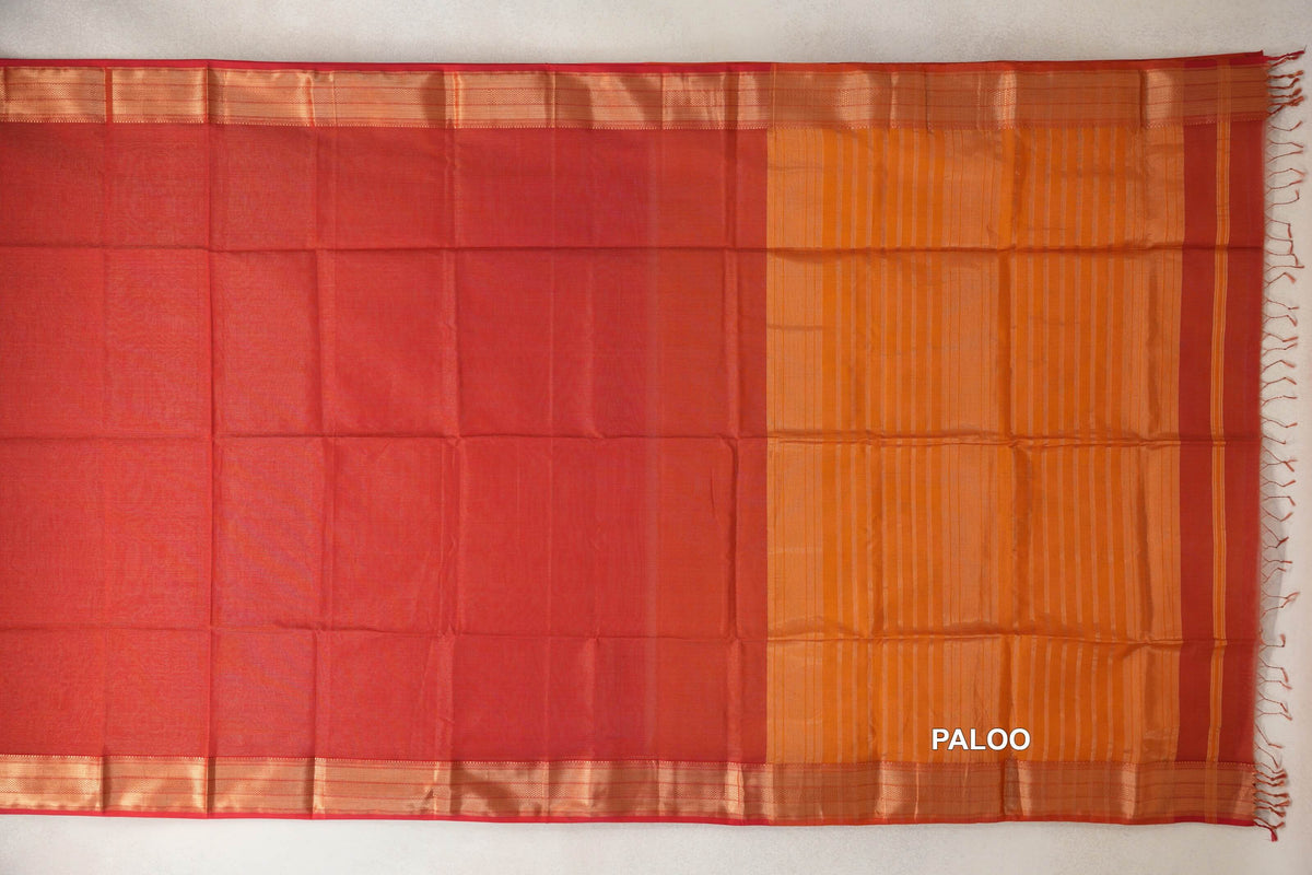 Tomato red Maheshwari silk cotton saree spread flat, with gold-toned woven border bands and a deep orange striped pallu with tassels.