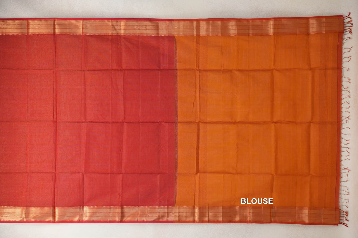 Maheshwari silk cotton saree laid flat, with a tomato red body, deep orange blouse section, striped borders and tassels along the right edge.