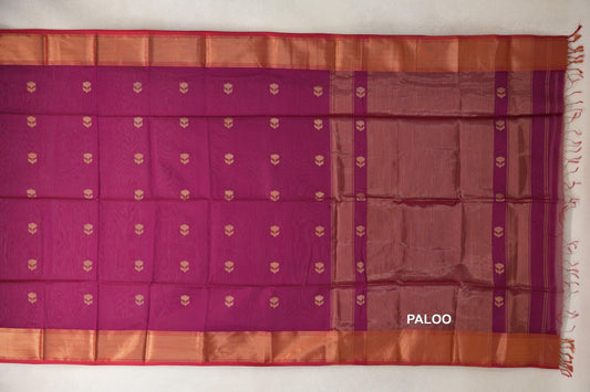 Reddish magenta Maheshwari silk cotton saree laid flat, with gold-toned floral motifs, copper-toned borders, pinkish red edges and a striped pallu with tassels.