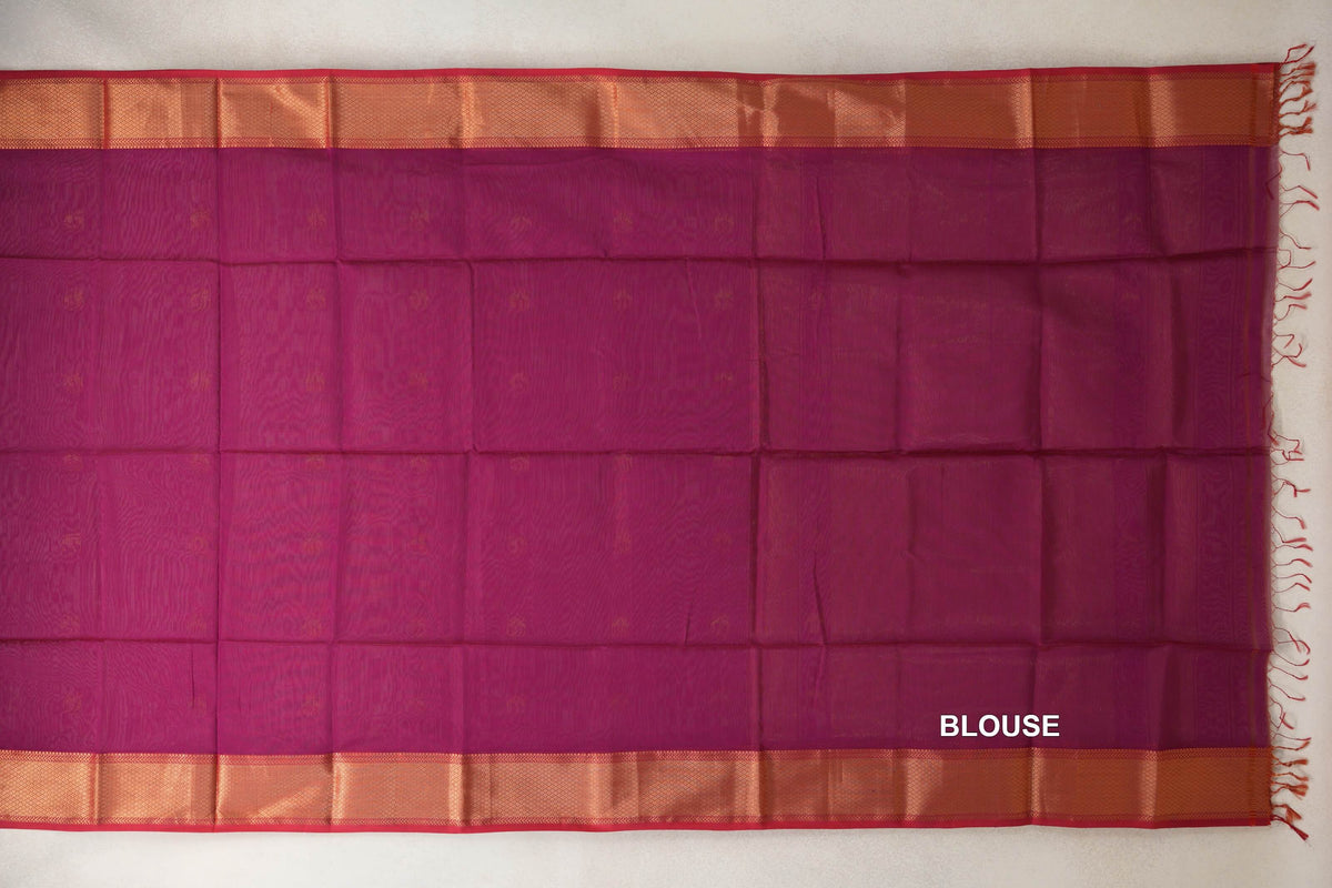 Reddish magenta Maheshwari silk cotton blouse fabric laid flat, with broad shimmering borders, pinkish red selvedge and tassels at one end.