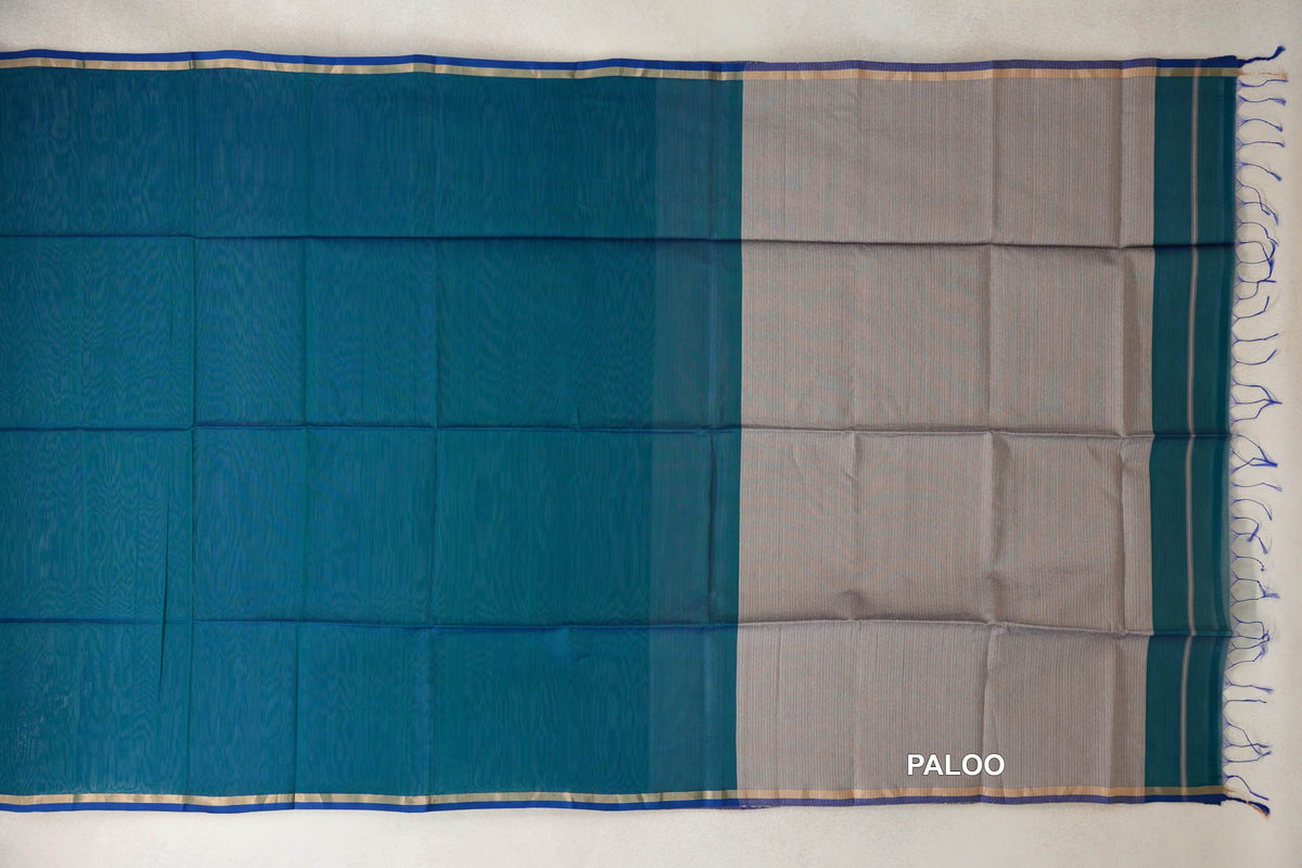 Maheshwari silk cotton saree laid flat, showing a peacock green body, peacock blue selvedge borders and a silver beige pallu with blue tassels.