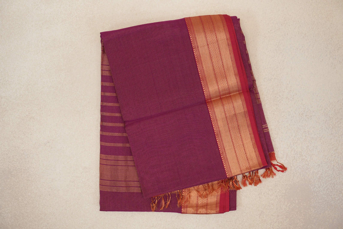 Folded deep magenta Maheshwari silk cotton saree with fine stripes, a broad patterned border, Rani Pink selvedge and tassels.
