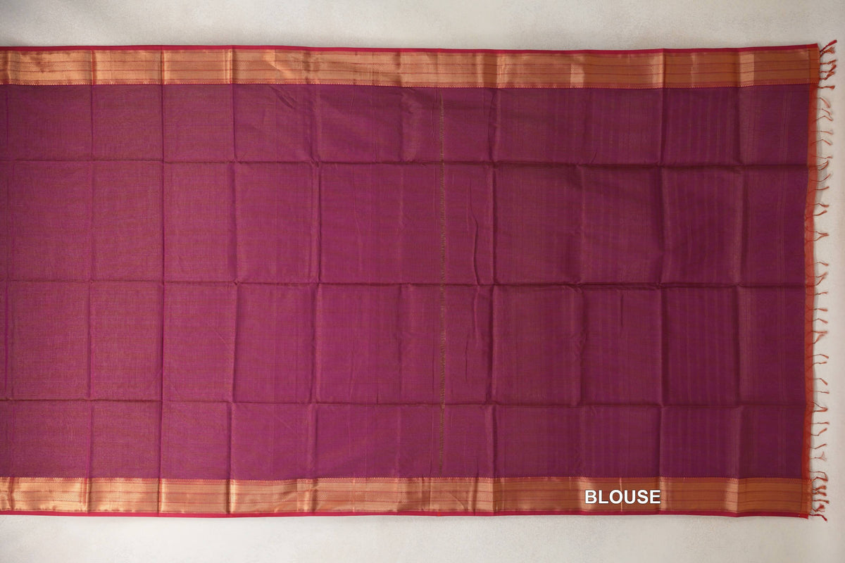 Deep magenta Maheshwari silk cotton blouse fabric laid flat, with copper-toned borders, Rani Pink edging and tassels along one side.