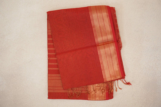 Folded tomato red Maheshwari silk cotton saree with fine gold stripes, a wide patterned gold border and tassels at one end.