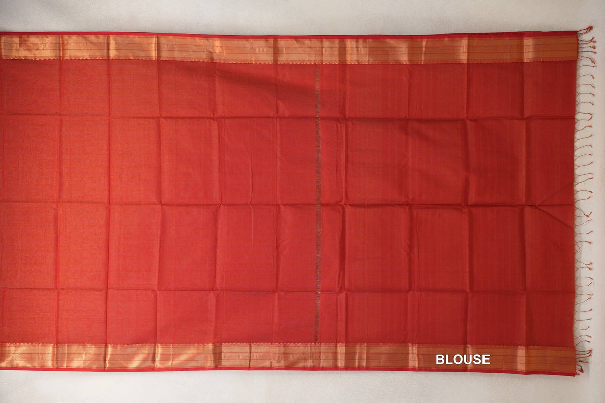 Tomato red Maheshwari silk cotton blouse fabric laid flat, with a plain body, gold-toned borders along both edges and tassels at one end.