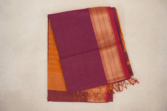Folded deep magenta silk cotton saree with fine stripes, a patterned border with rani pink selvedge, and deep orange fabric and tassels peeking out.