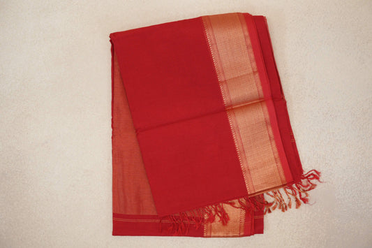 Folded vermilion red Maheshwari silk cotton saree with a finely striped body, patterned gold-toned border and tasselled end.