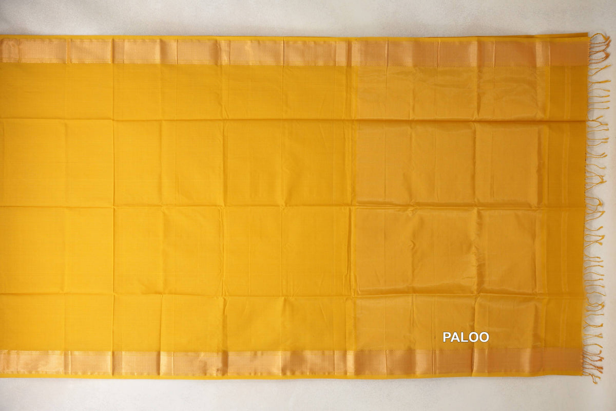 Turmeric yellow Maheshwari silk cotton saree spread flat, with a plain body, lustrous borders and a subtly striped pallu with tassels.
