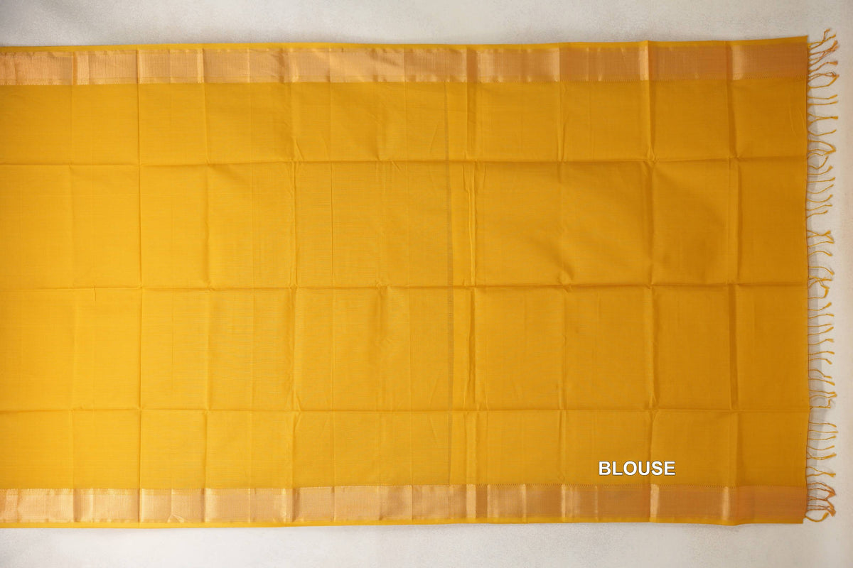 Turmeric yellow silk cotton blouse fabric laid flat, with lustrous borders along the top and bottom and tassels at one end.