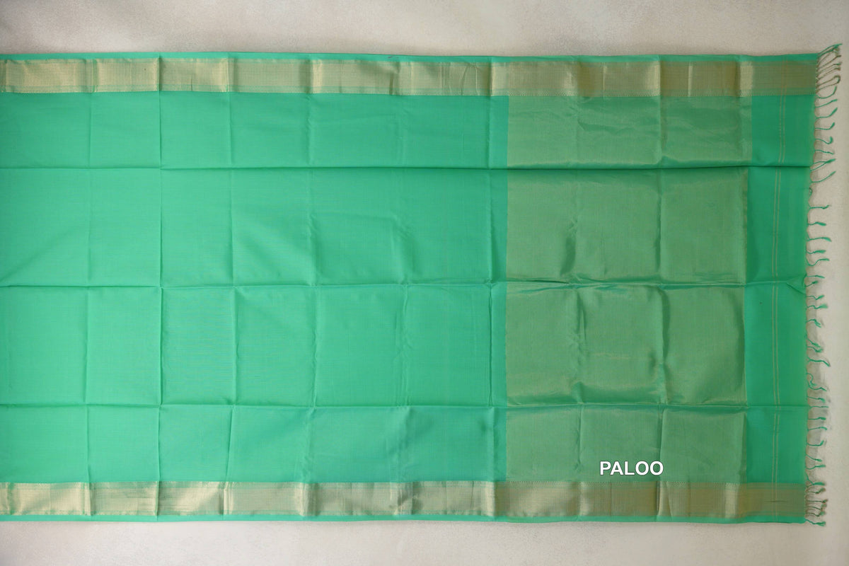 Sea green Maheshwari silk cotton saree laid flat, showing a plain body, pale gold-toned borders and a subtly striped pallu with tassels.