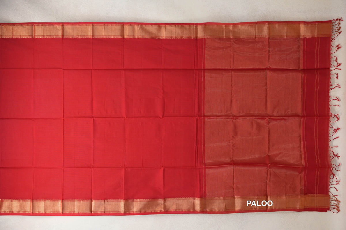 Vermilion red Maheshwari silk cotton saree spread flat, showing a plain body, gold-toned borders and a finely striped pallu with tassels.