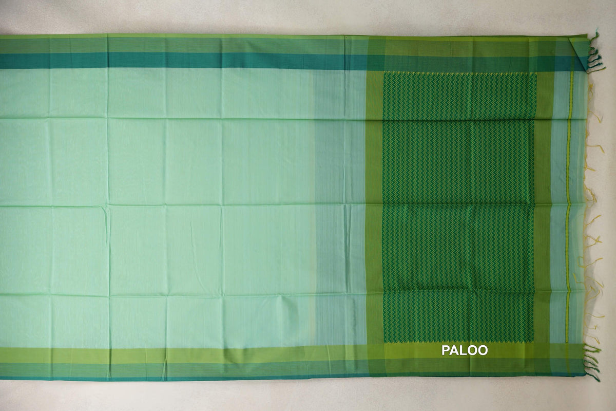 Mint green Maheshwari silk cotton saree laid flat, with parrot green and teal borders and a zigzag-patterned pallu with tassels.