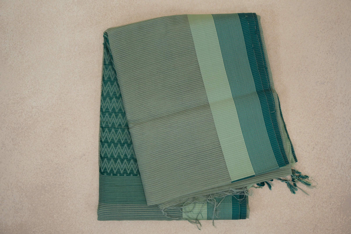 Folded pale sage green Maheshwari silk cotton saree with fine stripes, a light sage border, deep teal selvedge and tassels.