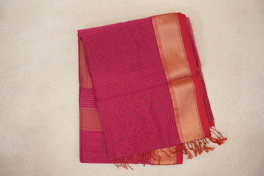 Folded bright magenta Maheshwari silk cotton saree with fine checks, a broad gold-toned border, deep magenta edge and tassels.