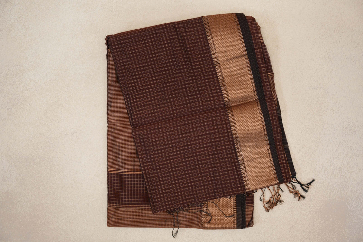 Folded coffee brown Maheshwari silk cotton saree with a fine check pattern, a wide woven border, deep coffee brown selvedge and tassels.