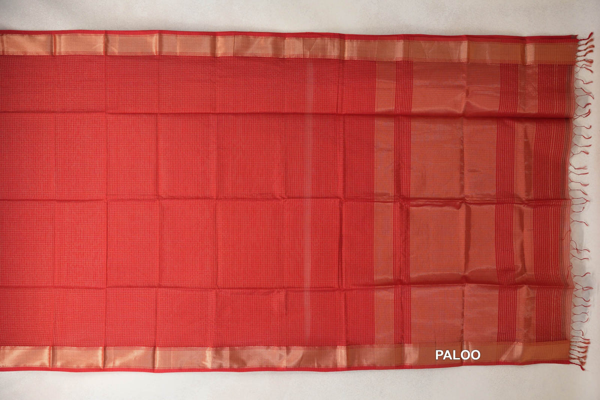 Tomato red Maheshwari silk cotton saree spread flat, showing a fine checked body, gold zari borders and a striped pallu with tassels.