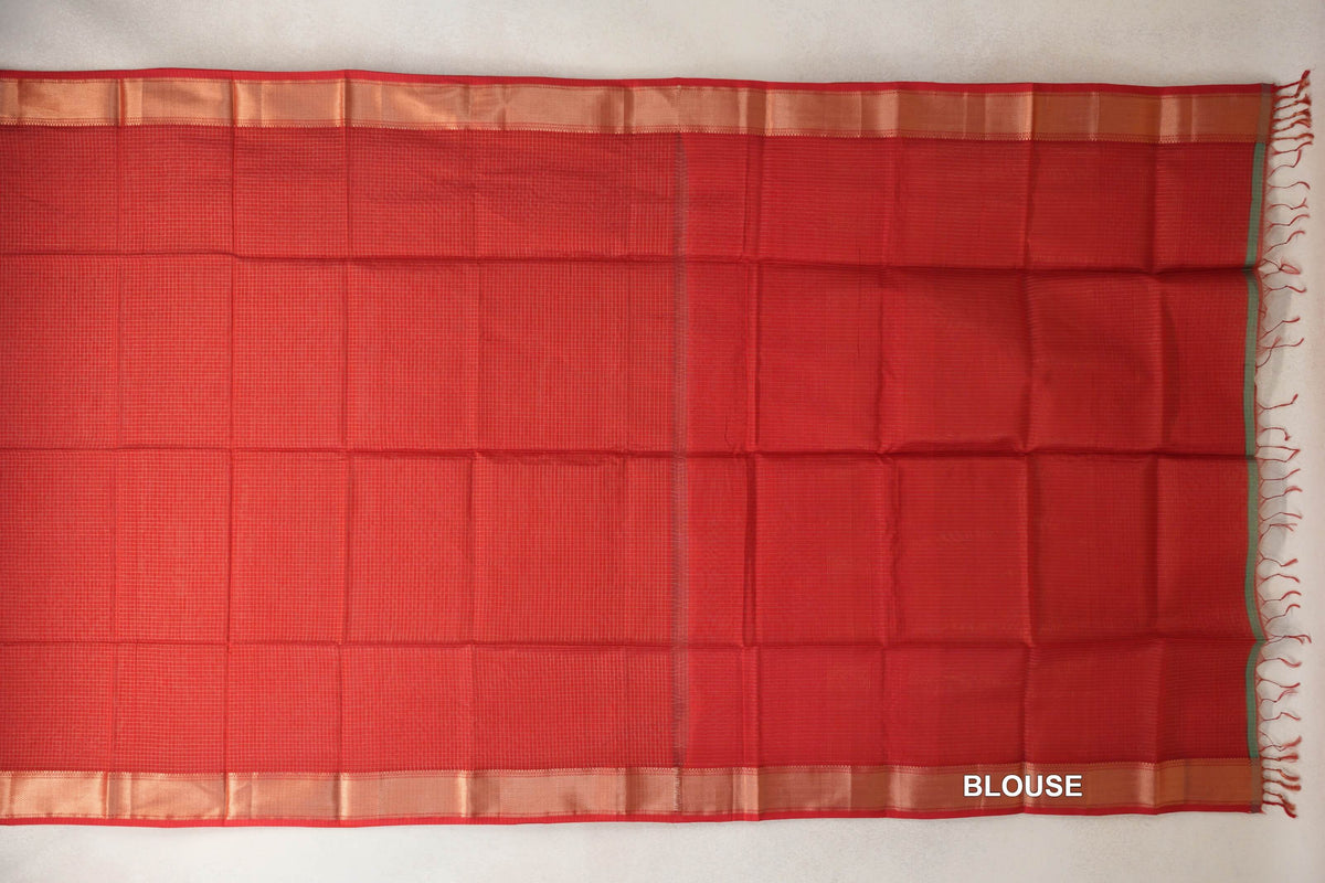 Tomato red Maheshwari silk cotton saree laid flat, showing a fine checked body, gold zari borders and a matching blouse section with tassels.