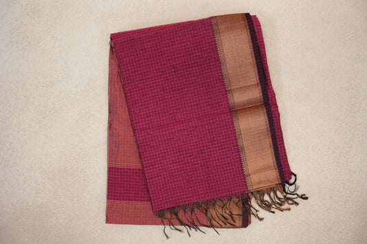 Folded Rani Pink Maheshwari silk cotton saree with a fine checked pattern, a broad copper-toned woven border, deep pink selvedge and tasselled ends.