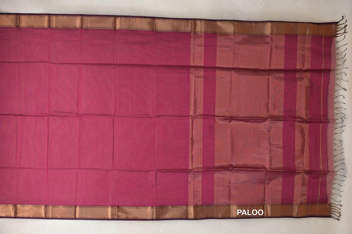 Rani Pink Maheshwari silk cotton saree spread flat, showing a fine checked body, copper-toned borders and a striped pallu with dark tassels.