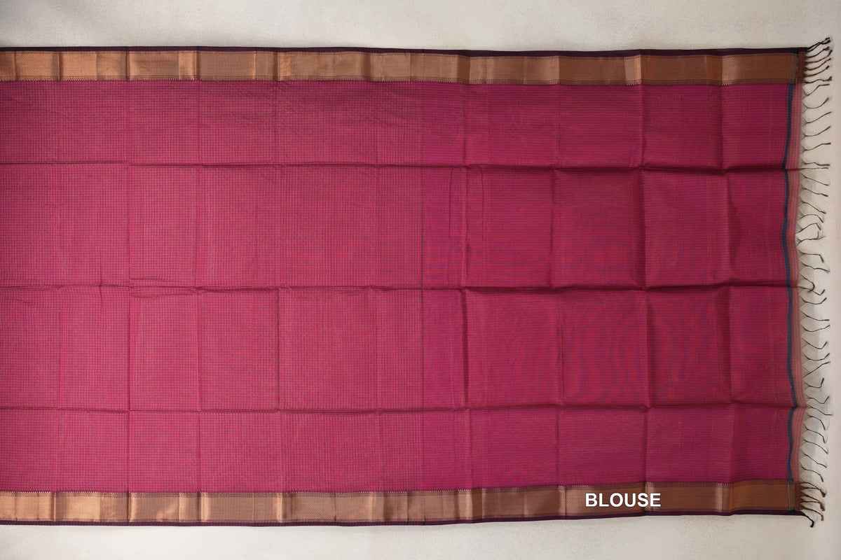 Rani Pink Maheshwari silk cotton blouse piece laid flat, with fine checks, copper-toned borders, deep pink selvedge and tassels at one end.