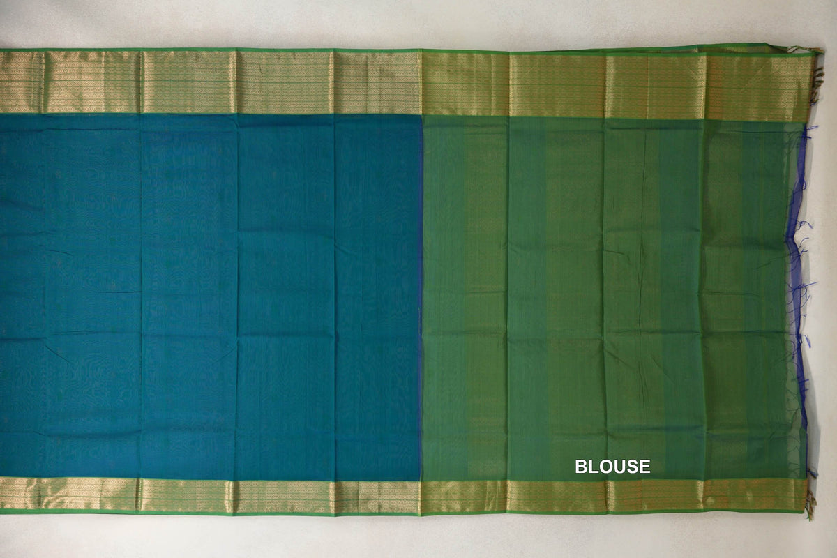 Teal blue Maheshwari silk cotton saree laid flat beside its leaf green blouse fabric, with gold-patterned leaf green borders along the top and bottom.