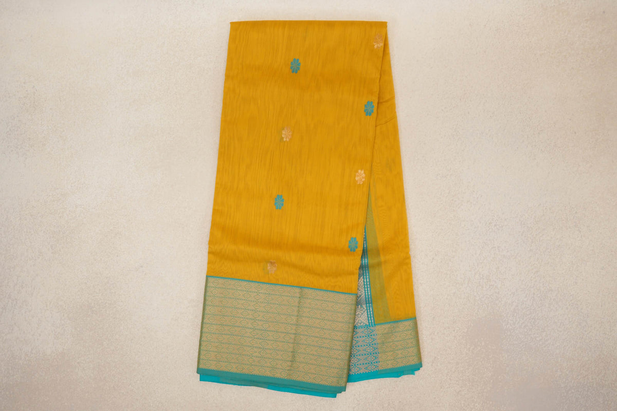 Folded mango yellow Maheshwari silk cotton saree with scattered turquoise and gold floral motifs and a wide, patterned turquoise blue border.