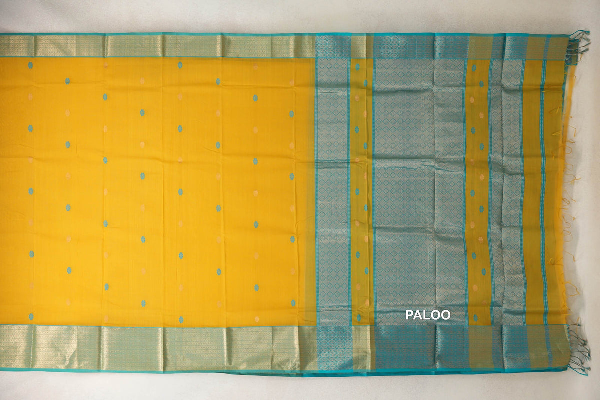 Maheshwari silk cotton saree laid flat, with a mango yellow body, small scattered motifs, and turquoise blue patterned borders and pallu with tassels.