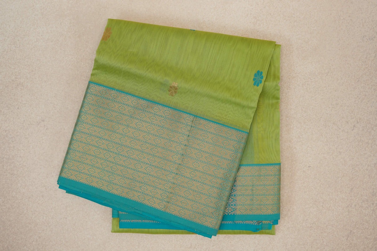 Folded Maheshwari silk cotton saree with a lime green body, small floral motifs and a turquoise blue border with gold-toned geometric patterns.
