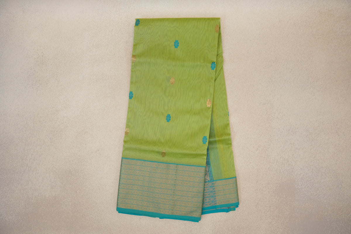 Folded lime green Maheshwari silk cotton saree with scattered turquoise and gold floral motifs and a turquoise blue geometric border.