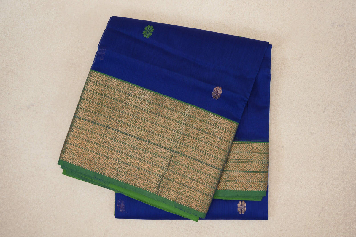 Folded Maheshwari silk cotton saree with a deep royal blue body, small scattered motifs and a wide forest green border with gold geometric patterns.